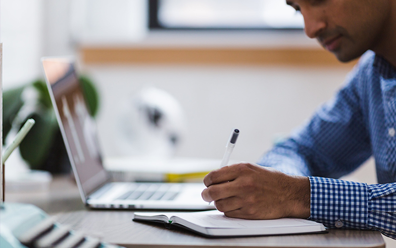 Student writing with a computer and pen